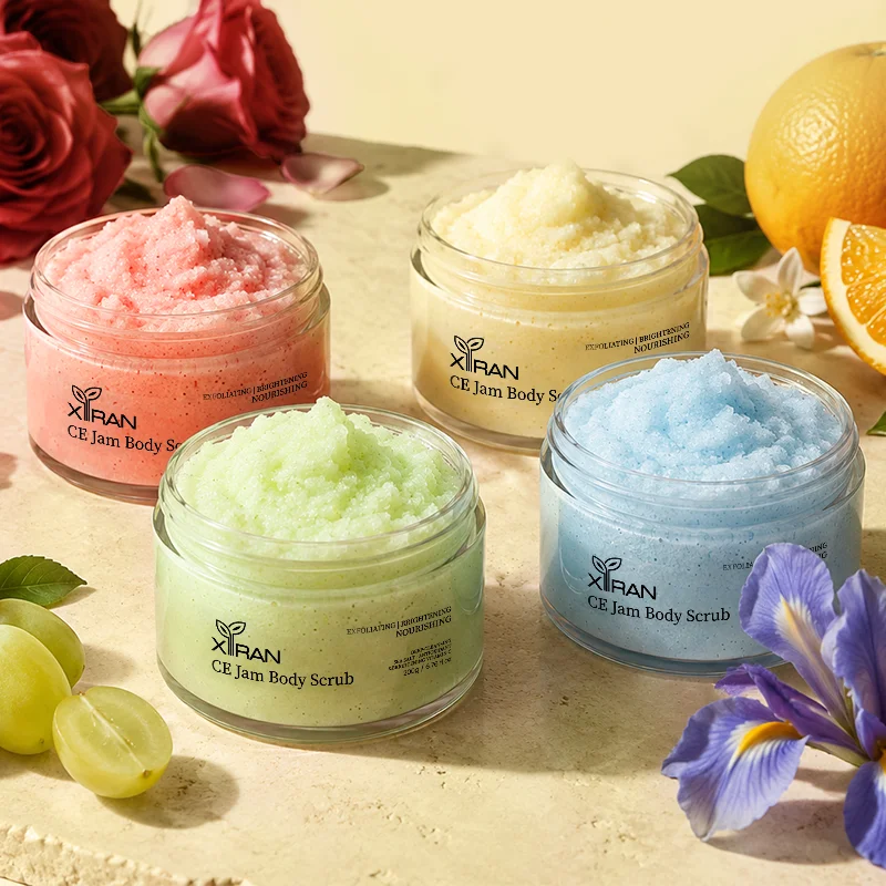 Four jars of XiRan CE Jam Body Scrub in red, green, yellow, and blue, surrounded by roses, grapes, and citrus fruits.